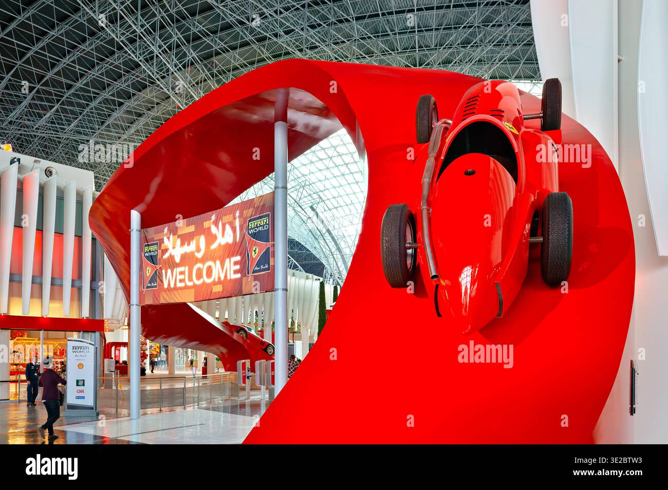 I visitatori entrano al Ferrari World di Abu Dhabi. Un modello Ferrari rosso è appeso sopra il cartello di benvenuto. La gente attraversa l'attrazione. Foto Stock
