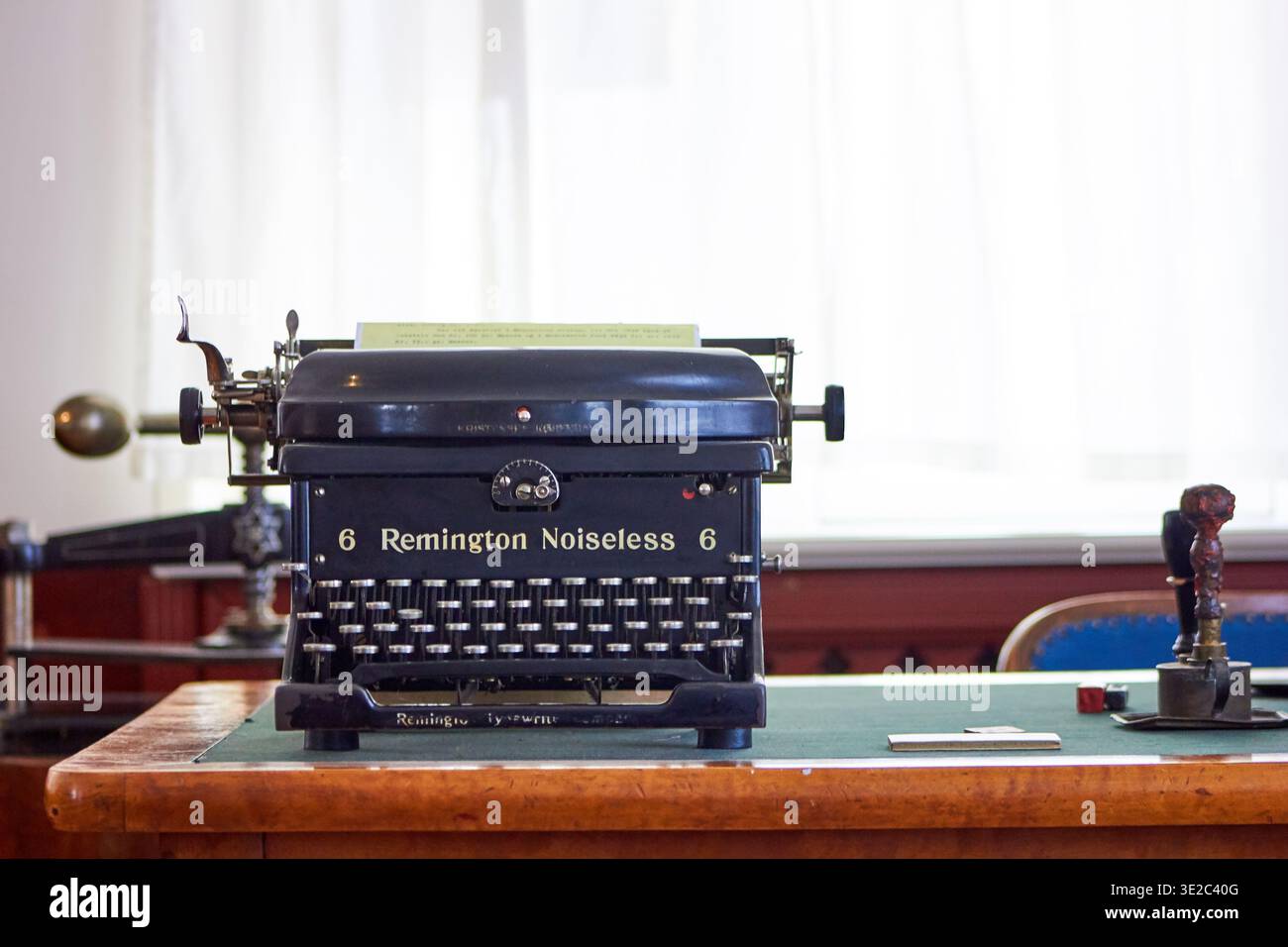Una macchina da scrivere Remington Noiseless 6 nera d'epoca si trova ben centrata su una scrivania in legno con un tappeto di feltro verde. L'antica meccanica... Foto Stock
