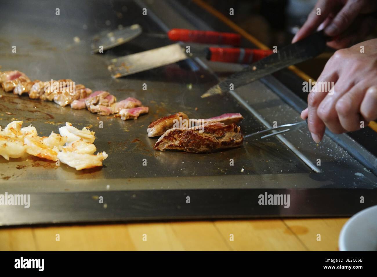 Le mani dello chef con la spatola sopra il teppanyaki. cucinare verdure, carne e pesce su un tavolo caldo per grigliate hibachi. Giapponese tradizionale. Spettacolo Teppan. cucina Foto Stock