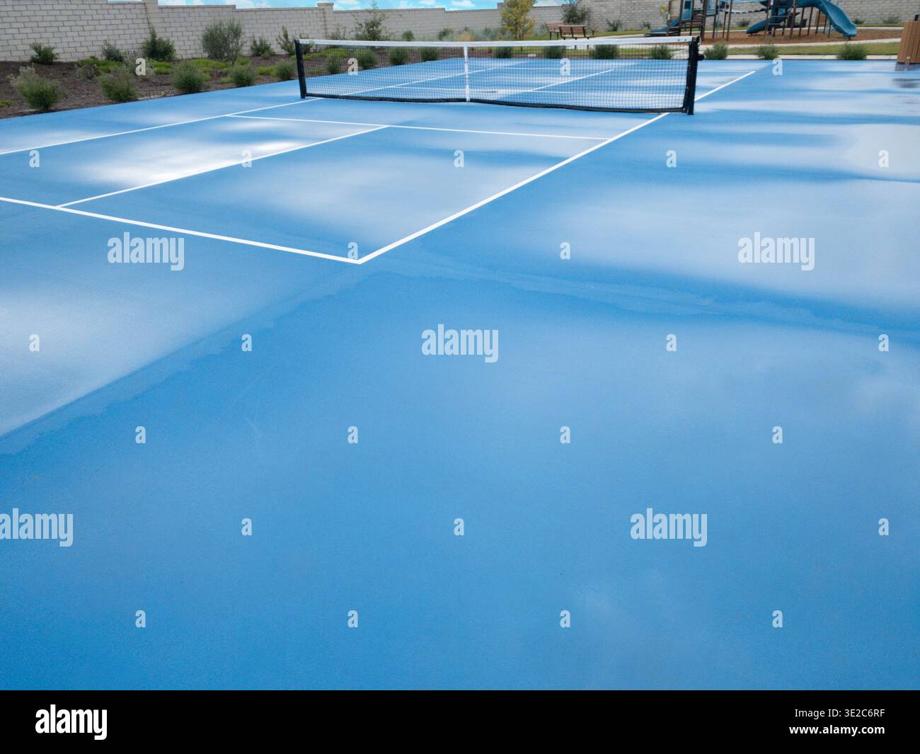 Campo da pallacanestro vuoto con superficie di gioco blu e rete in un parco pubblico all'aperto, con giardini circostanti, posti a sedere e strutture ricreative. Foto Stock
