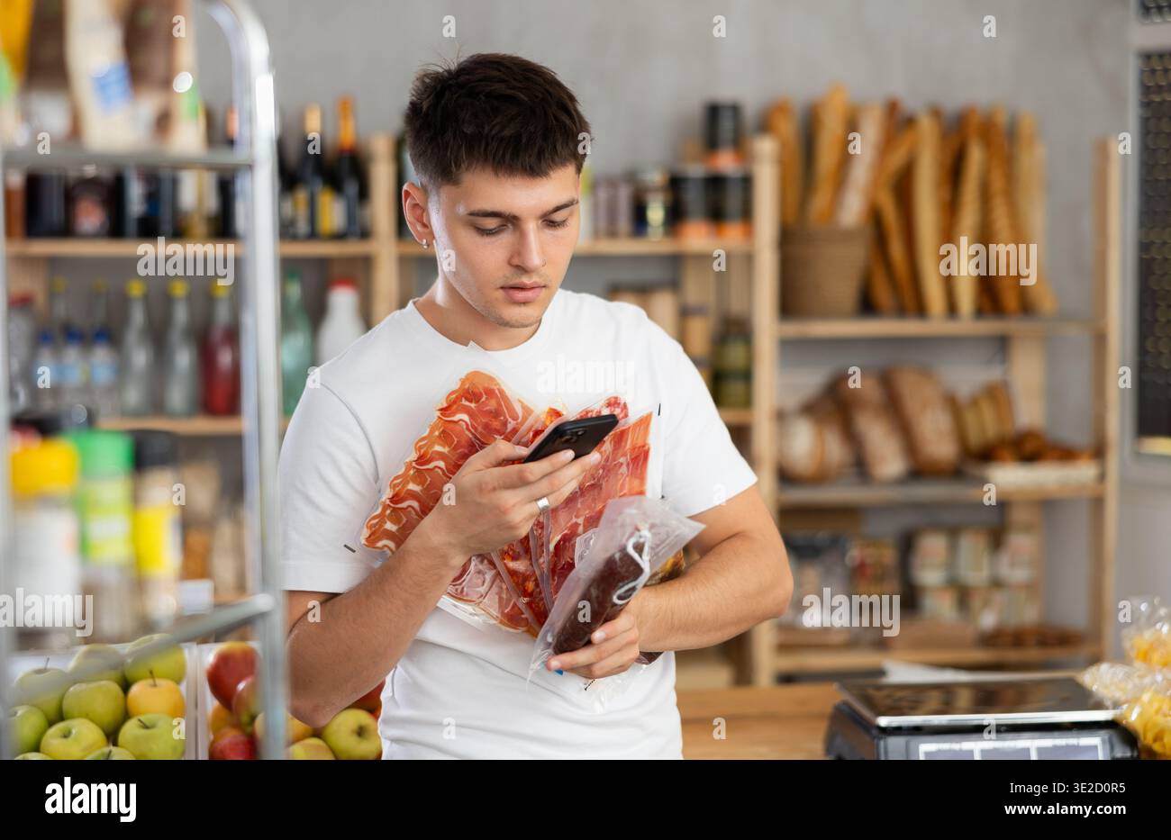 Acquirente positivo che esegue la scansione con il codice QR dello smartphone di salsiccia o carne secca nel supermercato Foto Stock