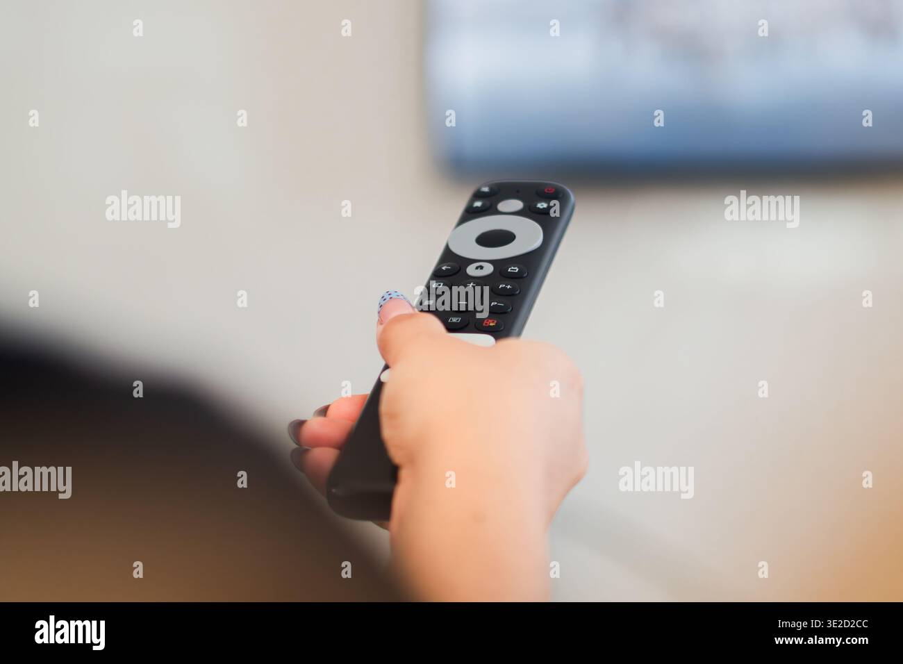 Primo piano della mano di una donna con un telecomando nero che punta sullo schermo TV, la casa intelligente e il concetto di streaming Foto Stock