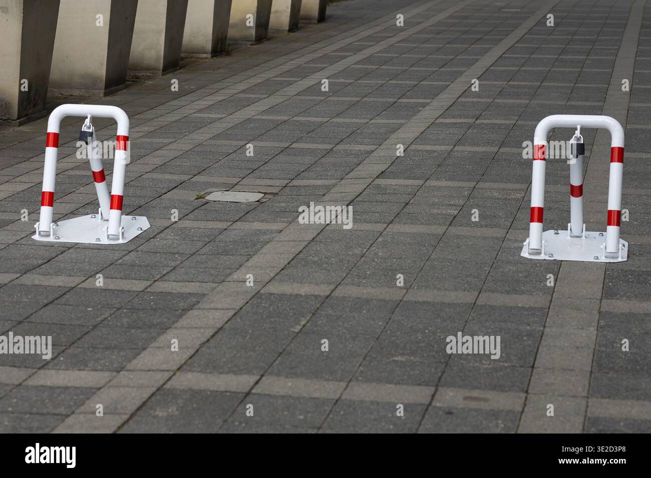 Due dissuasori bianchi e rossi con serrature integrate in piedi su un marciapiede di ciottoli grigio, che definiscono un'area di parcheggio protetta o una zona ad accesso limitato Foto Stock