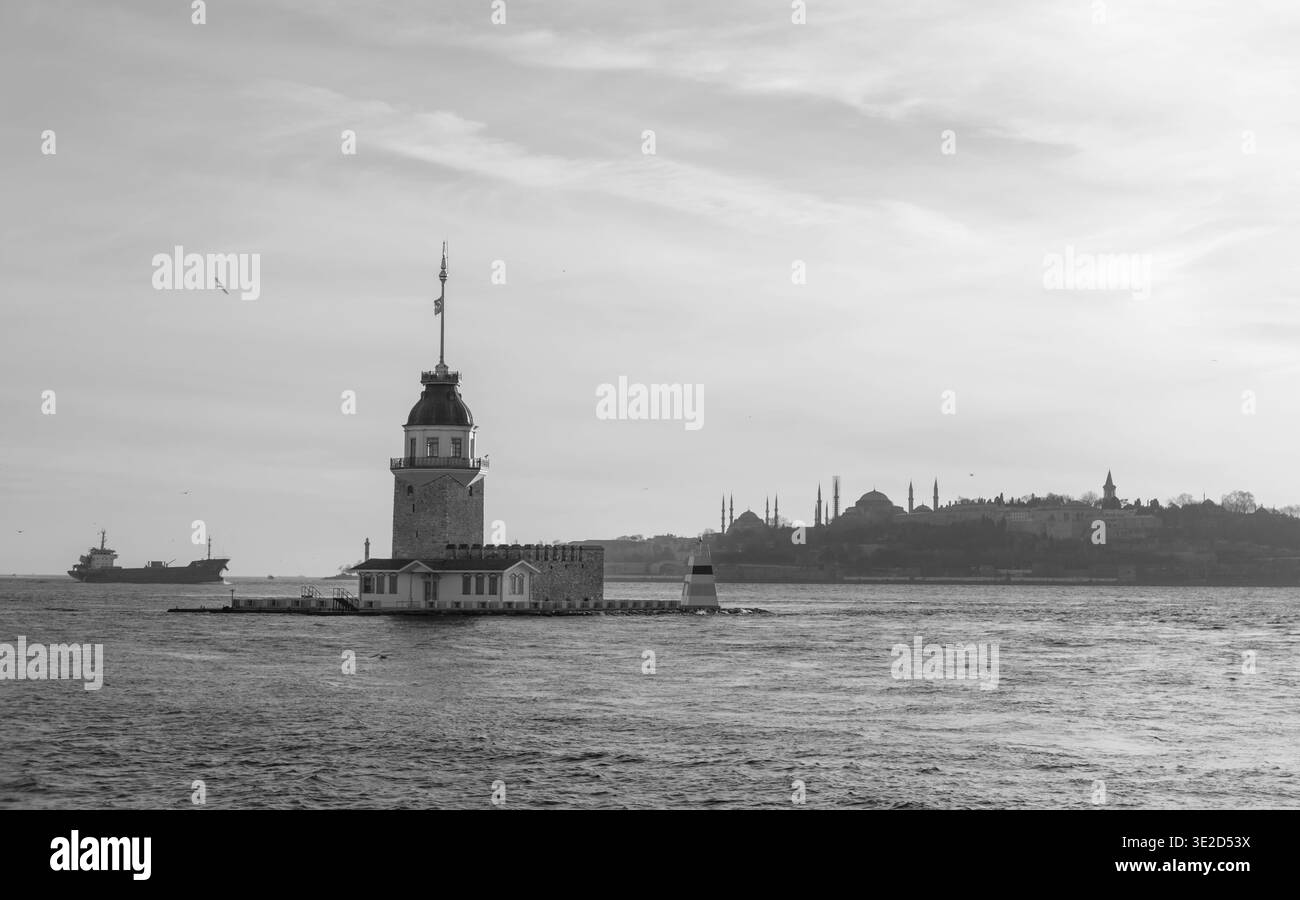 Vista monocromatica della Torre della Fanciulla sul Bosforo con lo skyline di Istanbul in lontananza dalla nave cargo in mare e l'ampio e suggestivo cielo che crea un tempo Foto Stock