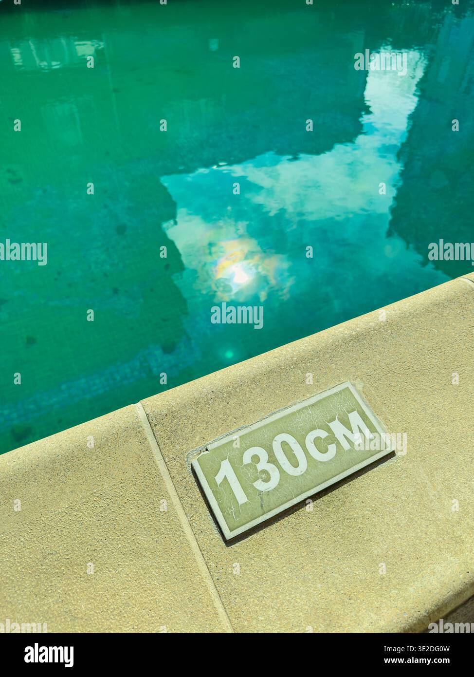 L'acqua della piscina riflette la luce del sole, mentre il marcatore di profondità mostra 130 cm. L'ambiente circostante suggerisce un ambiente residenziale con acque blu calme. Foto Stock