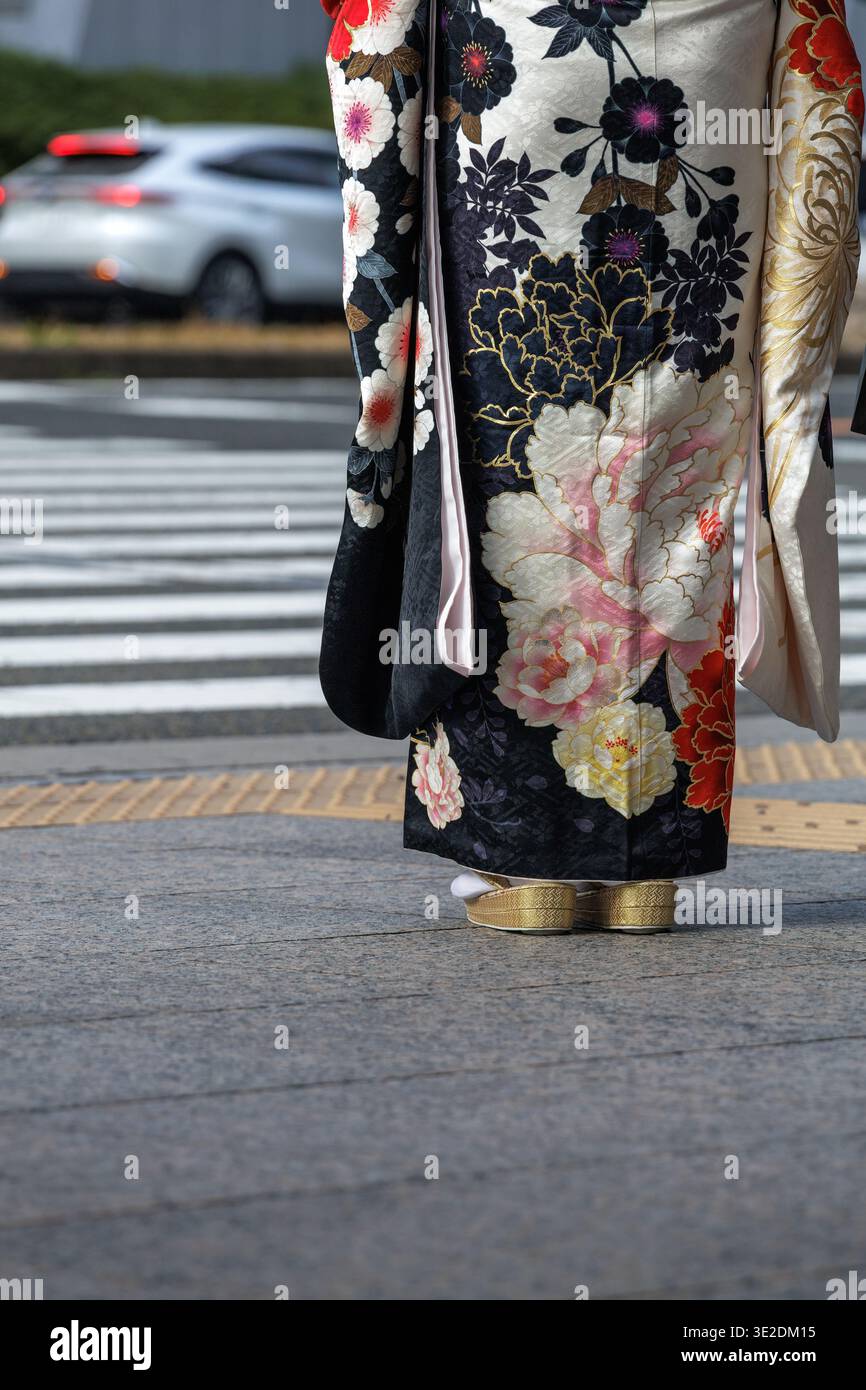 Donna in furisode bianco e nero con motivi floreali ornati e calze tabi bianche ben inserite in zori dorati in modo tradizionale. Foto Stock