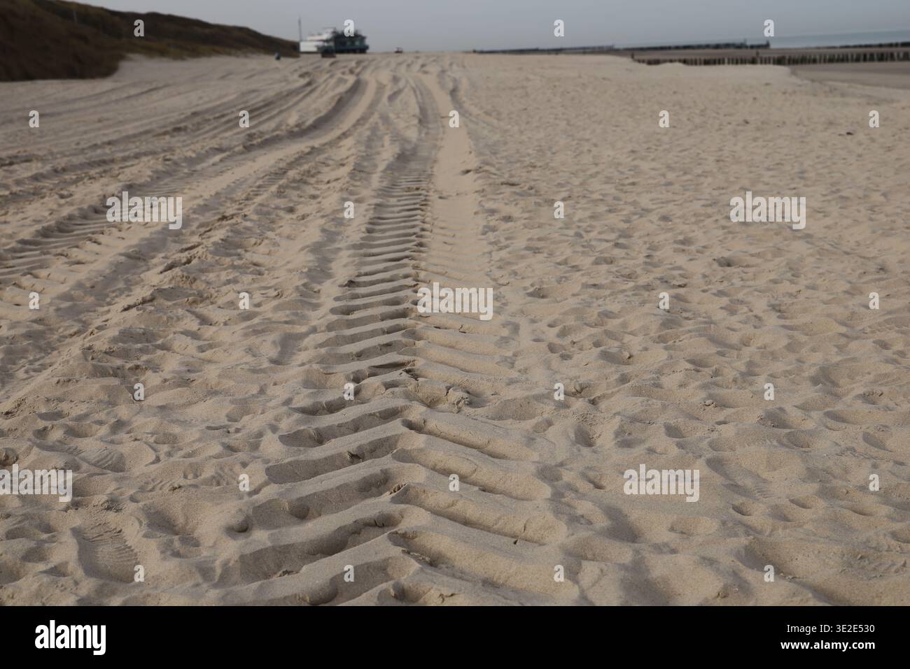 Le tracce di pneumatici sono di sabbia soffice su una spiaggia tranquilla, che porta in lontananza, fotografate con luce naturale, con un paesaggio costiero minimale e un cielo coperto. Foto Stock