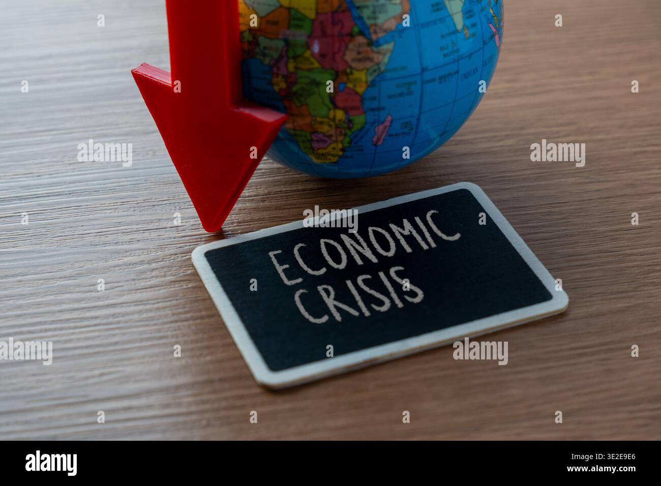 Un globo e una grande freccia rossa verso il basso accanto a una lavagna che legge la CRISI ECONOMICA. Recessione finanziaria globale, declino del mercato Foto Stock