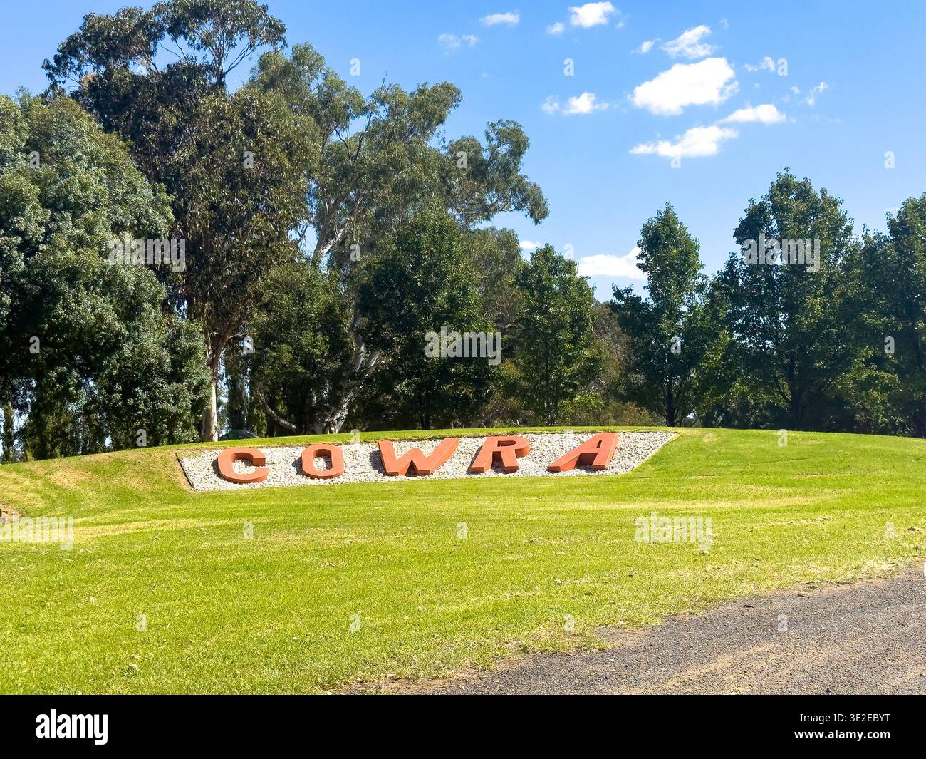 Cowra, NSW, Australia. 15 marzo 2026. - Un grande segno rosso che scrive "COWRA" è esposto su una collina erbosa ben curata, incorniciata da alberi verdi sotto una clea Foto Stock