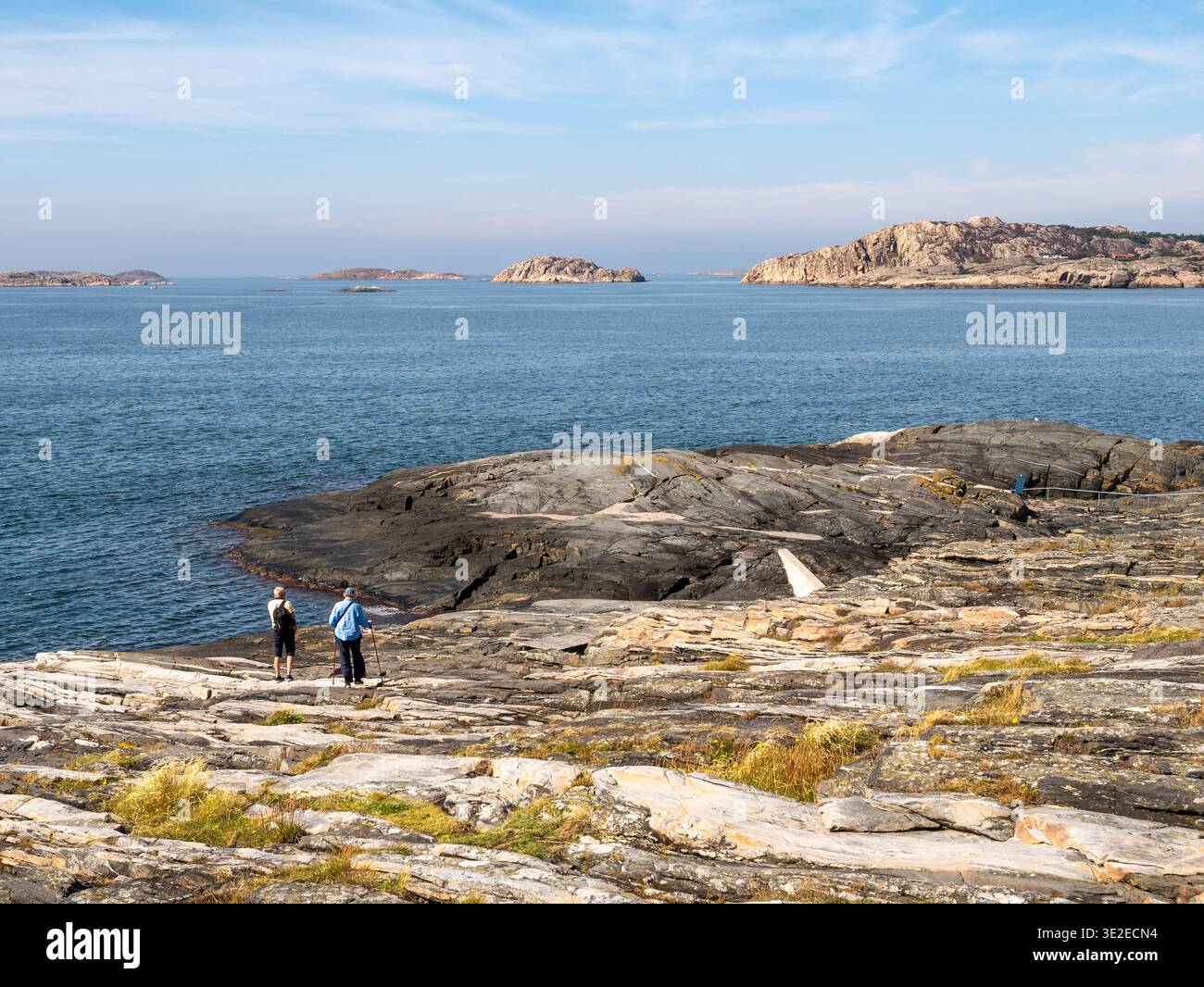 Due persone camminano sulla costa rocciosa di Åstol, Bohuslän, costa occidentale della Svezia, con mare aperto e piccole isole Foto Stock