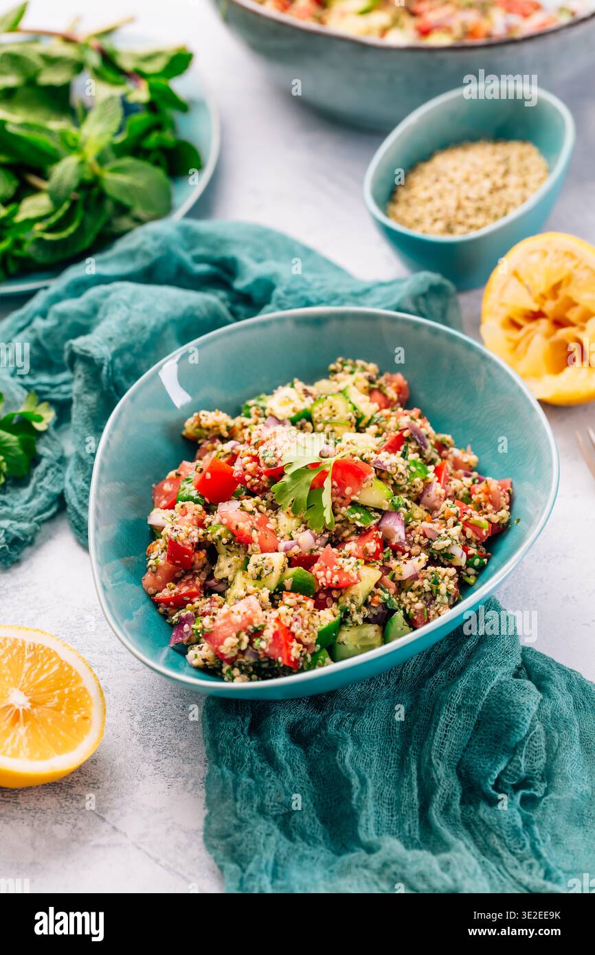 Insalata di couscous colorata con pomodori e cetrioli in un recipiente rustico, guarnita con menta fresca Foto Stock