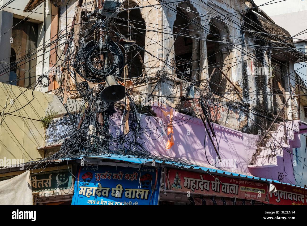 Un caotico groviglio di cavi e linee elettriche sospese precariamente sopra i negozi con la colorata segnaletica hindi nella città di Bundi. Foto Stock