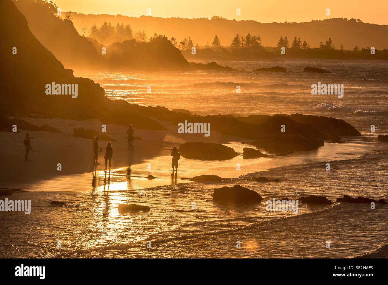 Tramonto dorato sulla spiaggia di Byron Bay con silhouette e riflessi sulla sabbia bagnata. Foto Stock