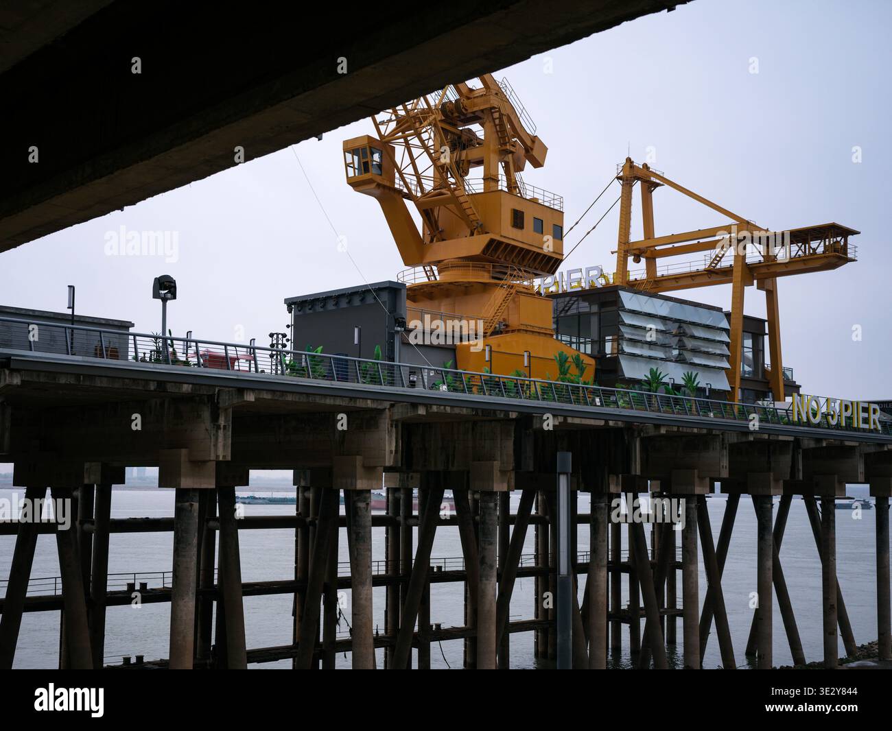 Wuhan, Cina - 4 marzo 2025: Vista ravvicinata di una gru industriale gialla e di un macchinario di carico su una struttura di pontile in legno. L'immagine acquisisce il mecc Foto Stock