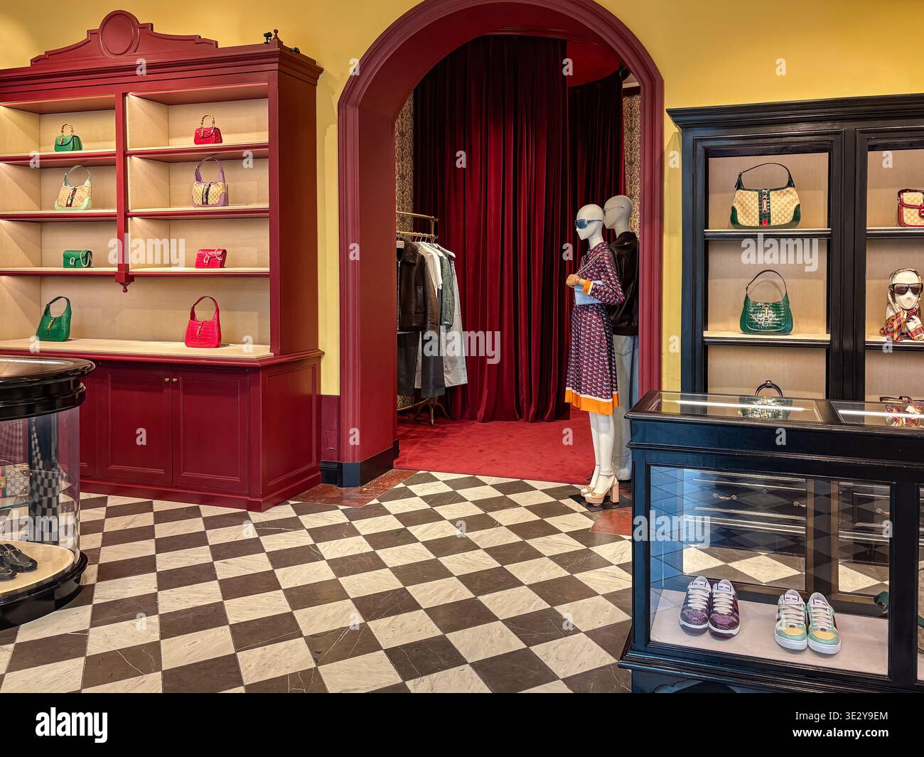 Interni boutique Gucci a Firenze, Italia, con borse di lusso su scaffali rossi e manichini su pavimento in marmo bianco e nero. Foto Stock