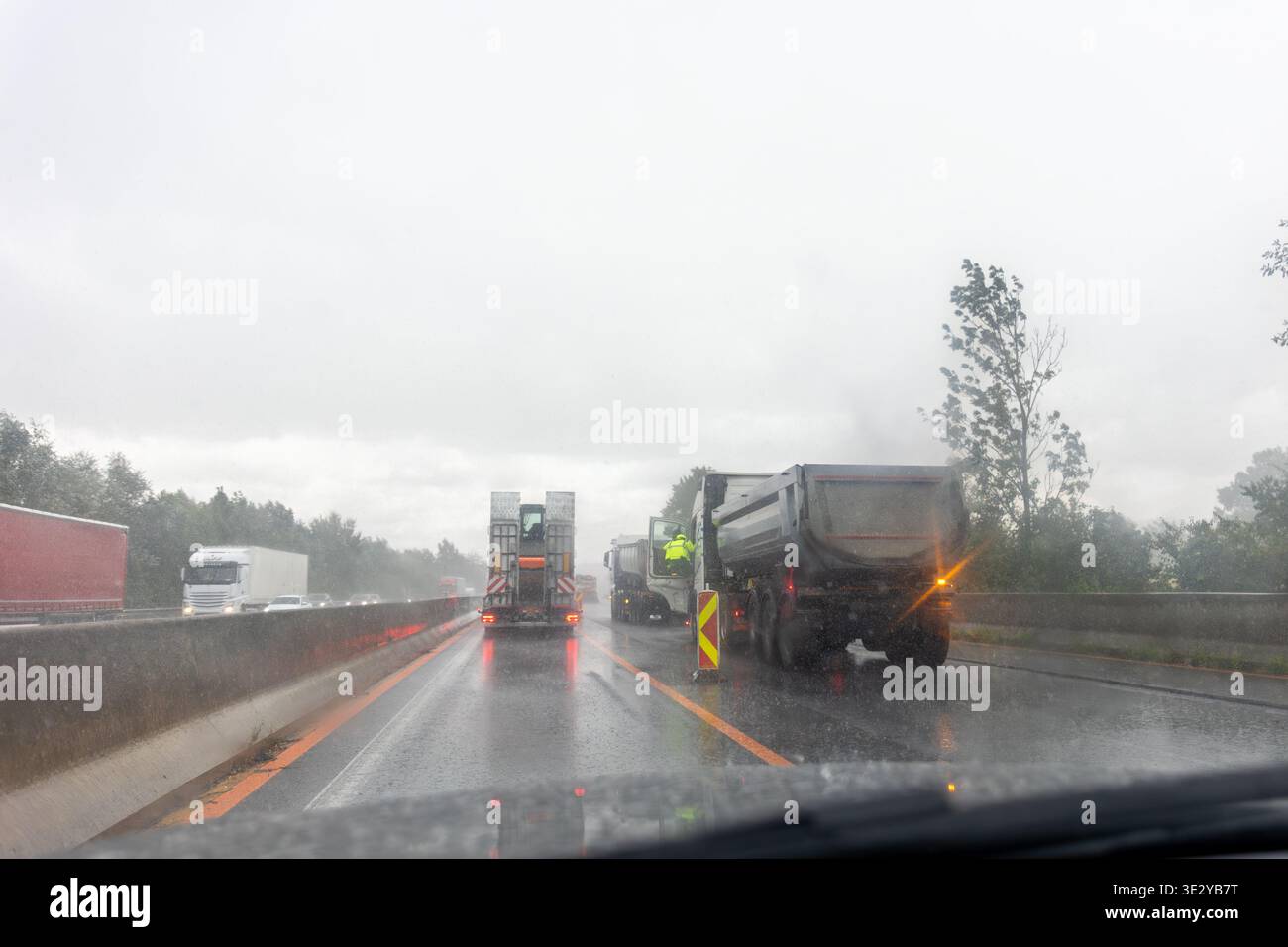 Conducente POV autocarri stradali stradali con pioggia i lavoratori indossano dispositivi di sicurezza traffico scarsa visibilità condizioni di asfalto bagnato. I veicoli si muovono lentamente Foto Stock