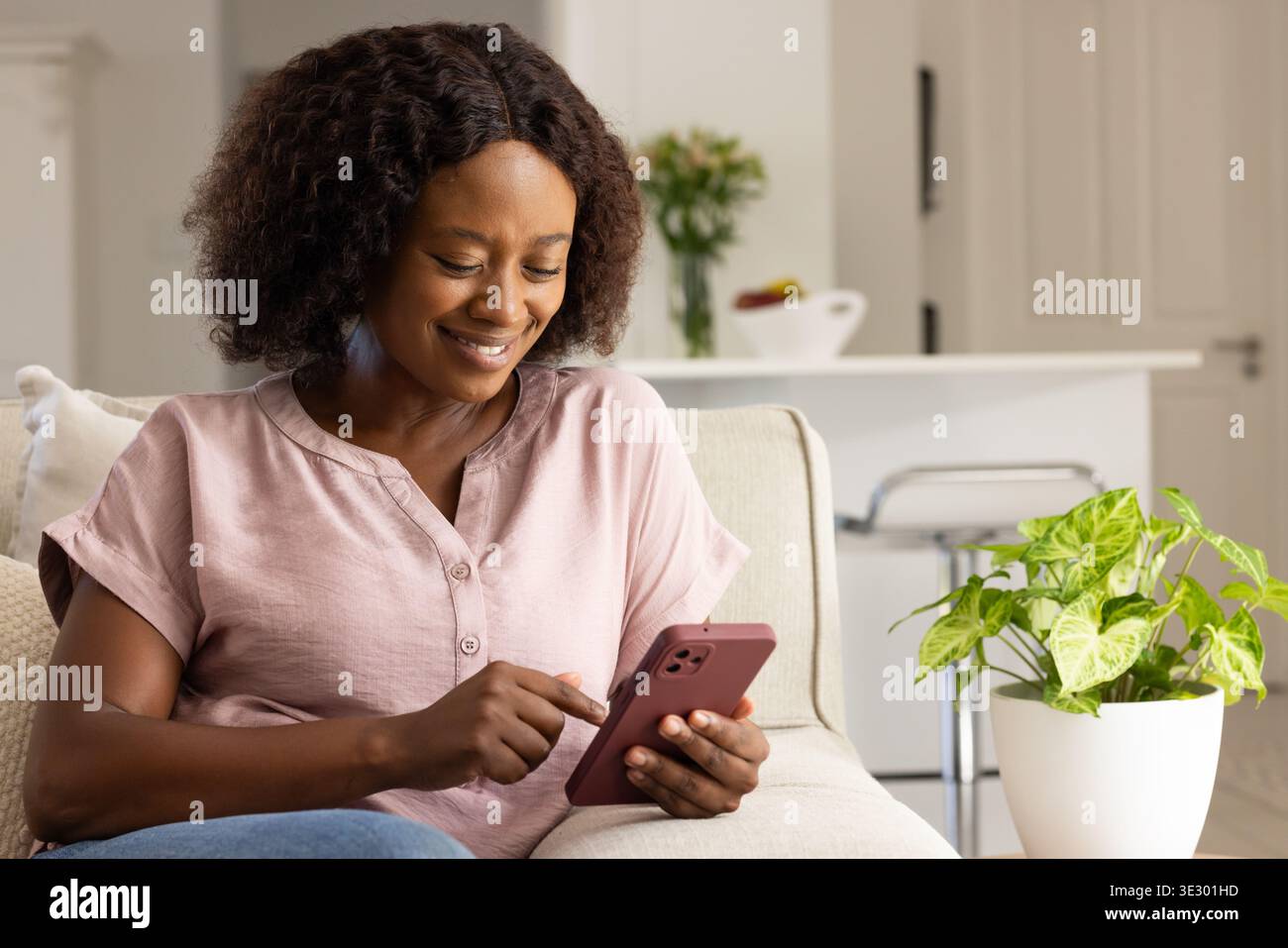 Donna adulta seduta sul divano di casa, tocca lo smartphone dopo la notifica, risponde ad un amico Foto Stock
