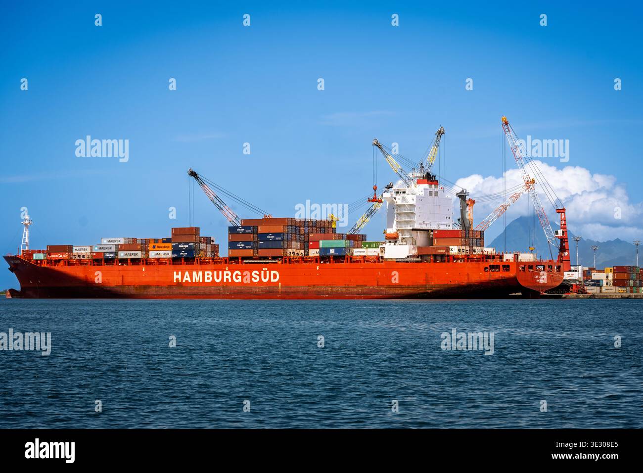 Papeete, Tahiti, Polinesia francese--2 febbraio 2023. Una massiccia nave da carico, la Hamburg Süd, è ormeggiata in un porto affollato, con gru impegnate attivamente Foto Stock