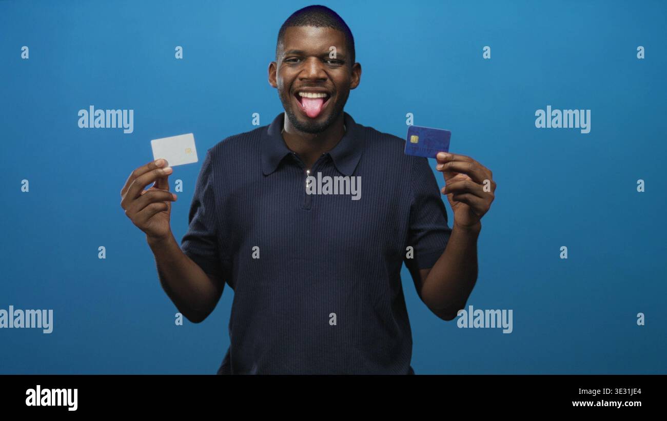 Giovane con due carte di credito, linguetta a occhi chiusi che le presenta sullo sfondo blu dello studio; scelta giocosa. Foto Stock