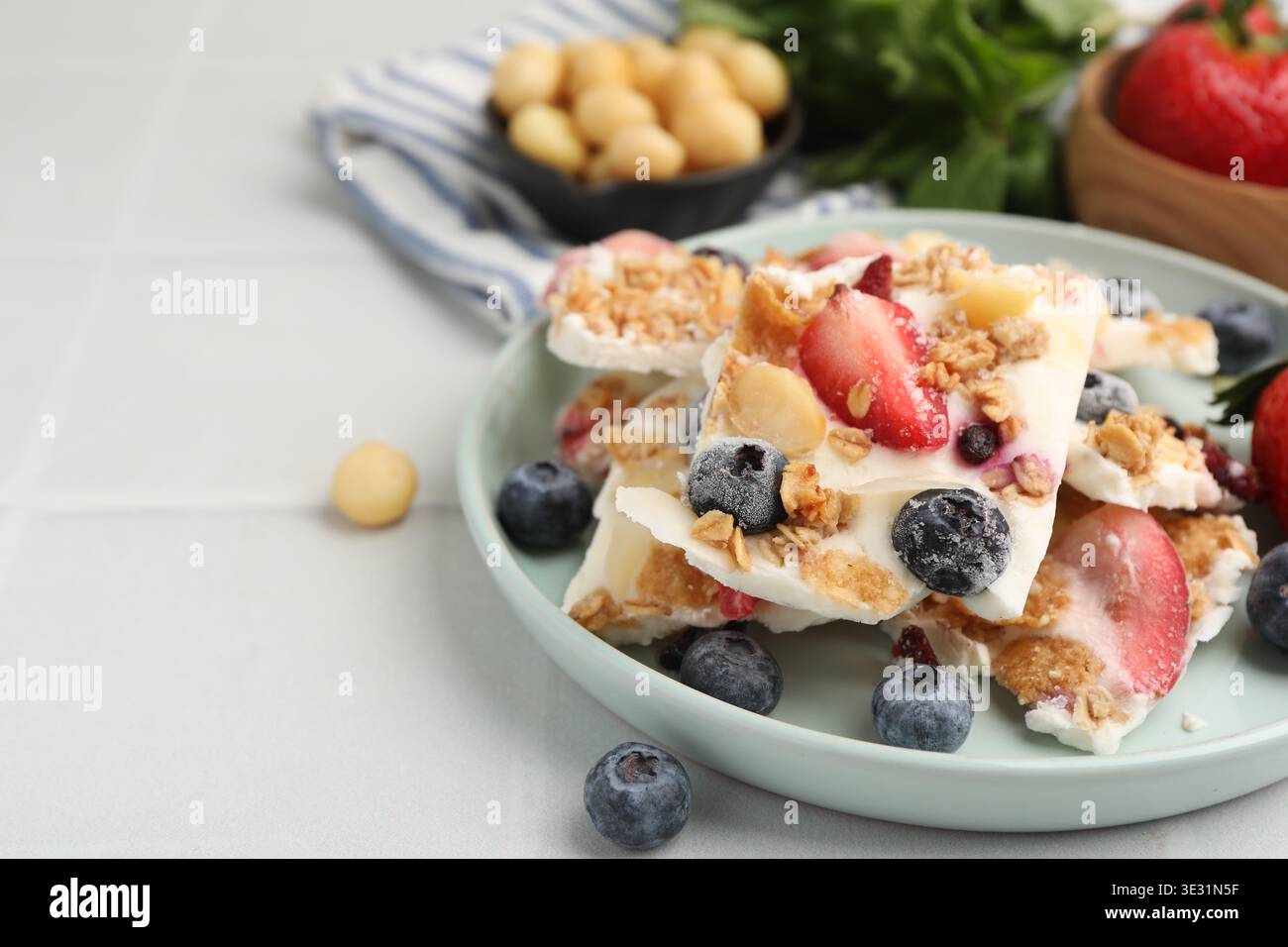 Pezzi di gustosa corteccia di yogurt con frutti di bosco e muesli su un tavolo piastrellato leggero, primo piano. Spazio per il testo Foto Stock