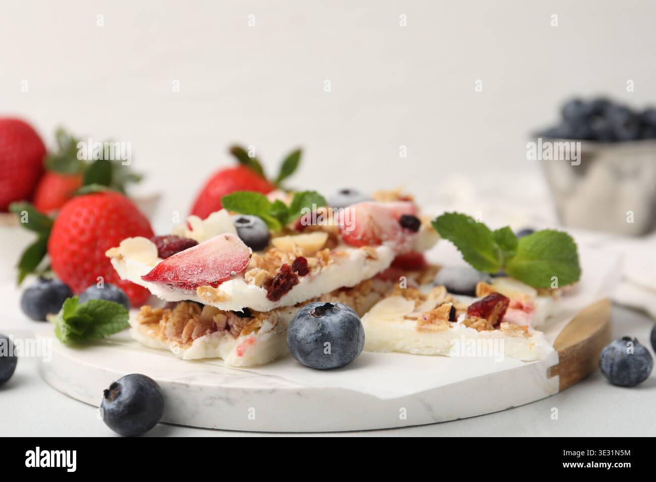 Pezzi di gustosa corteccia di yogurt con frutti di bosco, muesli e menta sul tavolo leggero, primo piano Foto Stock