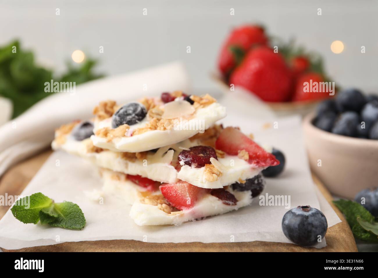 Pezzi di gustosa corteccia di yogurt con frutti di bosco, muesli e menta sul tavolo su sfondo grigio, primo piano Foto Stock