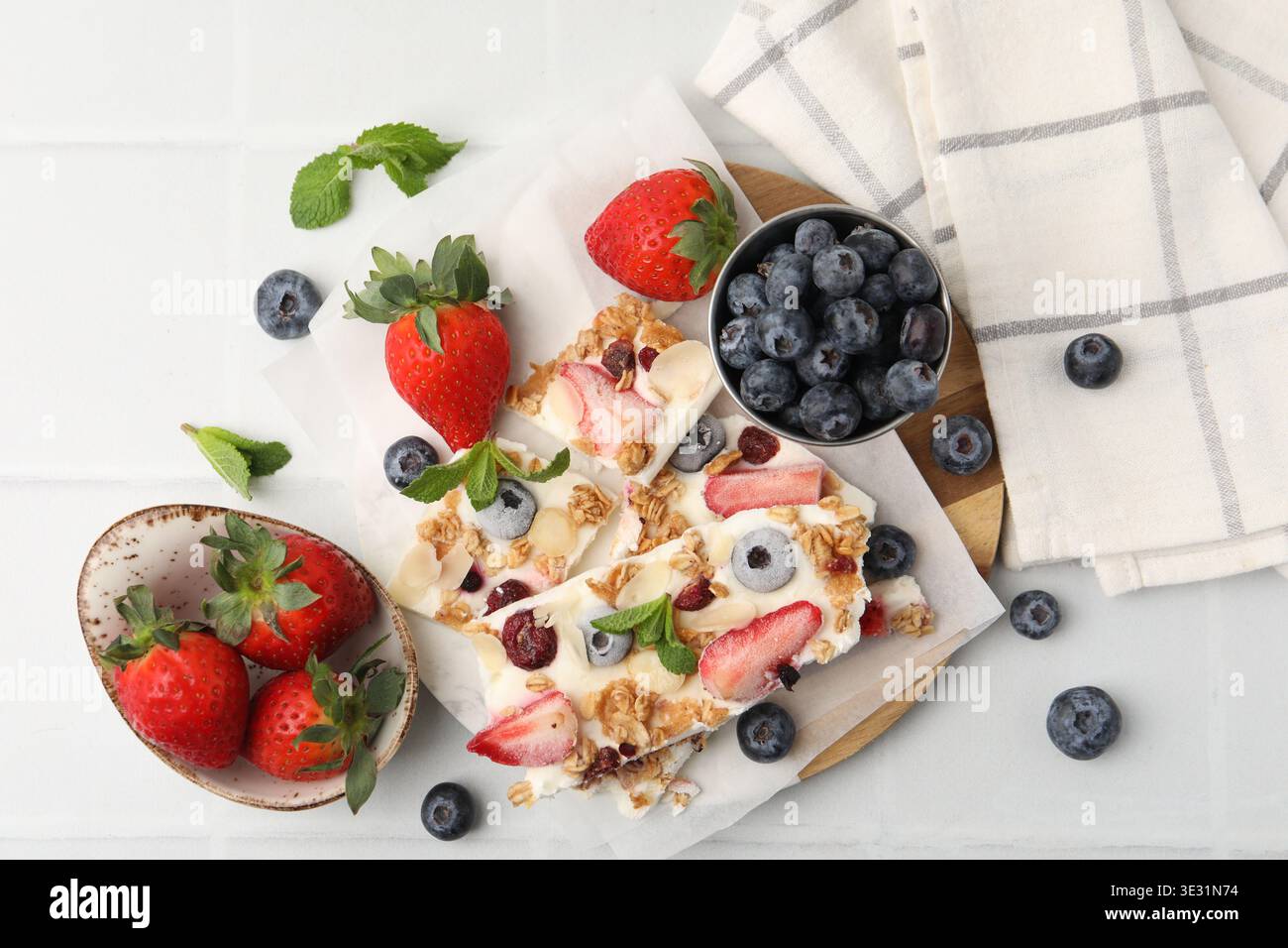 Pezzi di gustosa corteccia di yogurt con frutti di bosco, muesli e menta su un tavolo piastrellato leggero, in piano Foto Stock