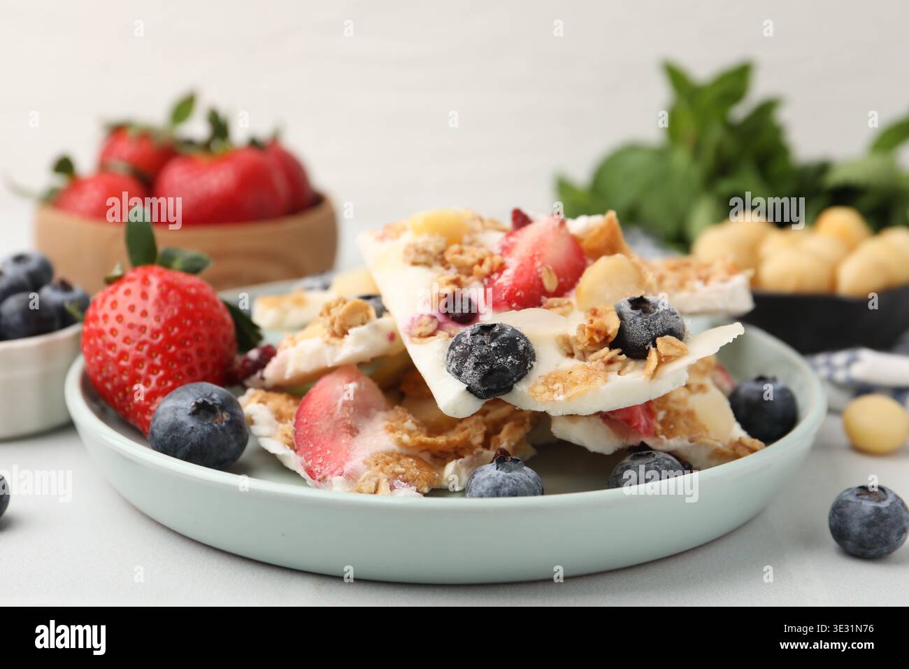 Pezzi di gustosa corteccia di yogurt con frutti di bosco e muesli sul tavolo leggero, primo piano Foto Stock