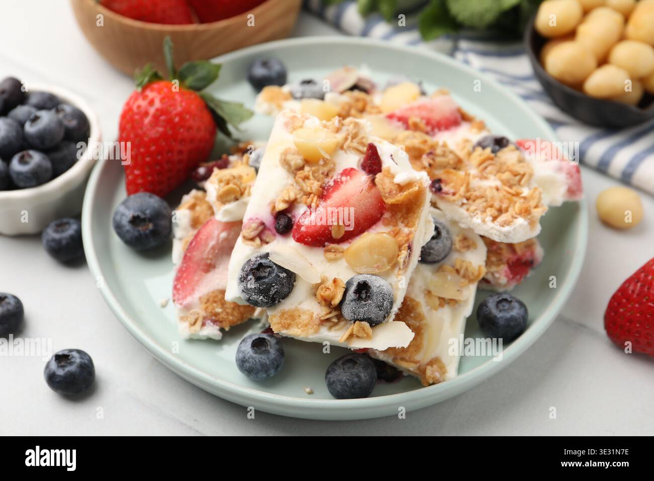Pezzi di gustosa corteccia di yogurt con frutti di bosco e muesli sul tavolo leggero, primo piano Foto Stock