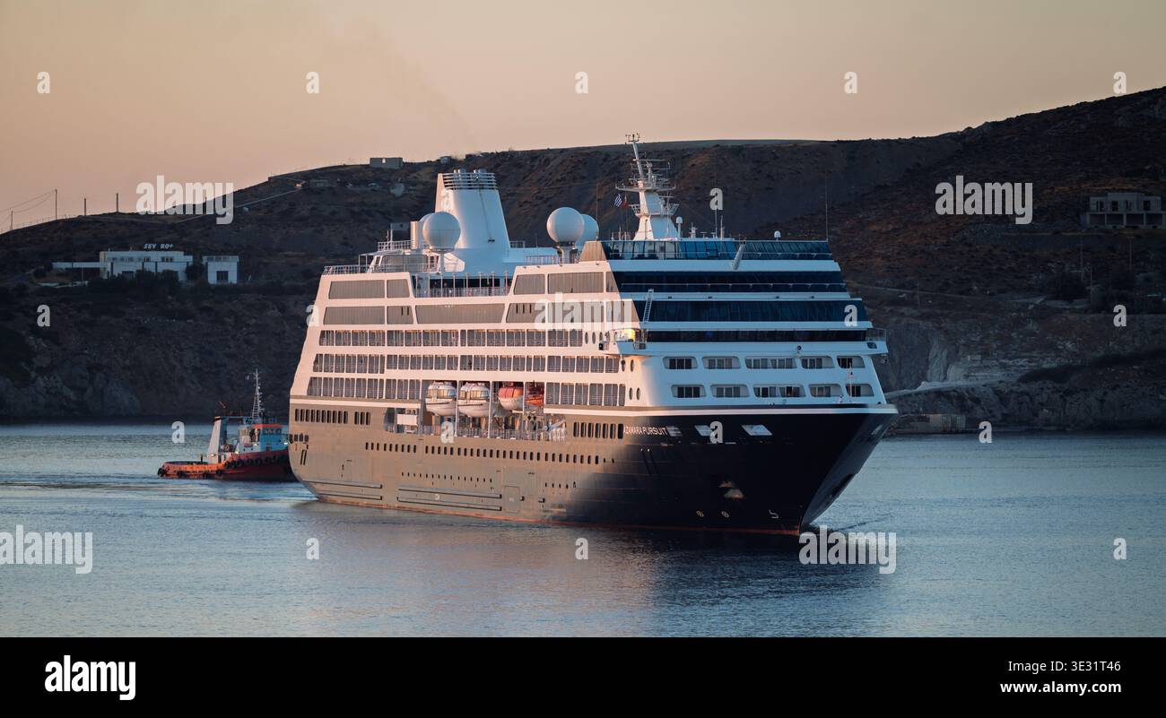 Grande nave da crociera assistita da rimorchiatore nel porto mediterraneo con sfondo roccioso sulle colline Foto Stock