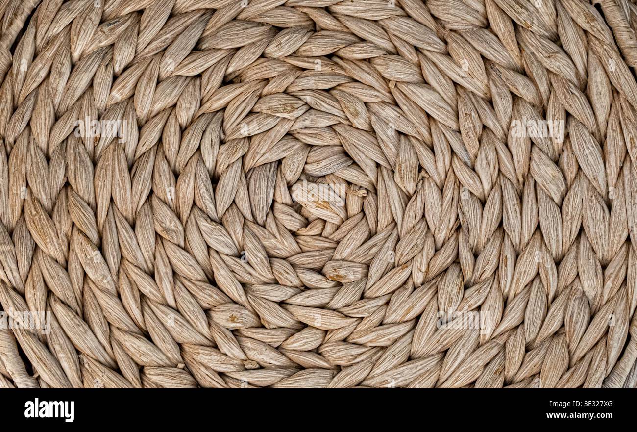 Primo piano di una superficie in fibra naturale intrecciata ermeticamente disposta con un motivo a spirale circolare. La texture organica presenta tonalità beige e abbronzatura calde con vi Foto Stock