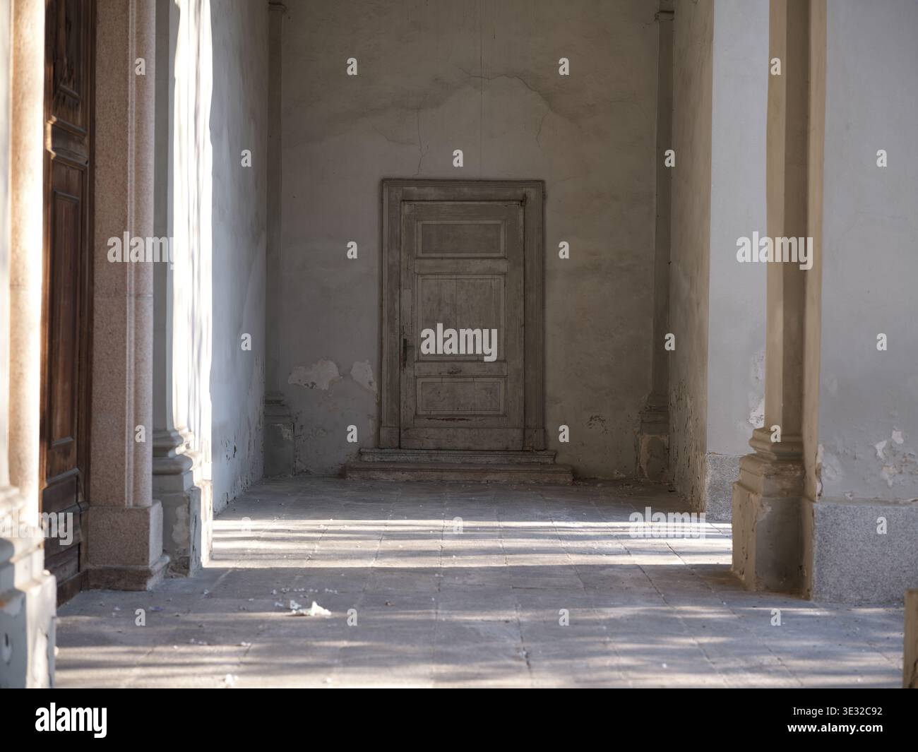 Porta in legno intemprata all'interno di un interno in decadenza con pareti staccate e texture usurate, evocando abbandono, silenzio e il passare del tempo. Foto Stock