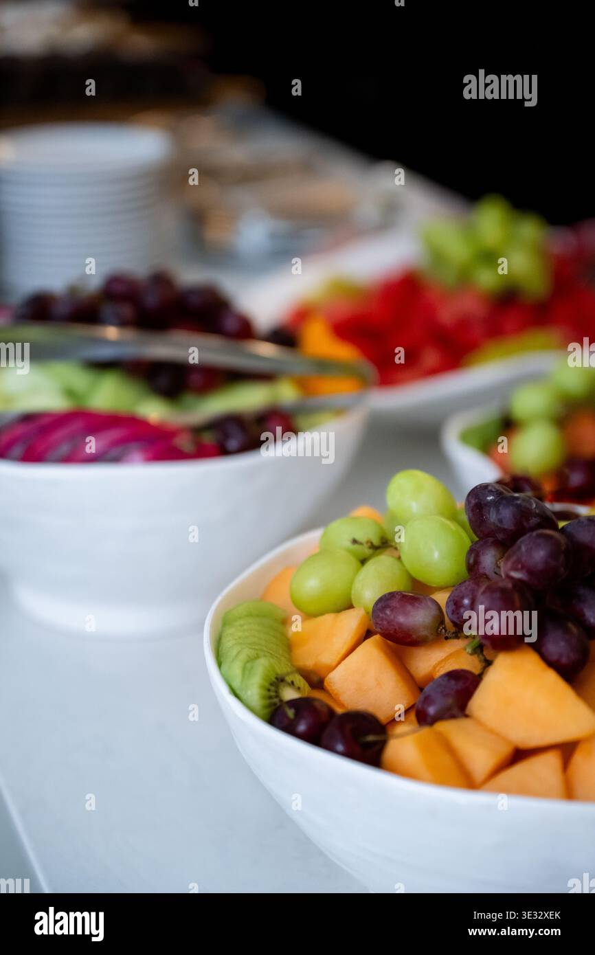 Ciotola per insalata di frutta fresca con uva, melone e kiwi al tavolo a buffet. Insalata di frutta colorata con uva verde e rossa, cantaloupe e kiwi a fette Foto Stock