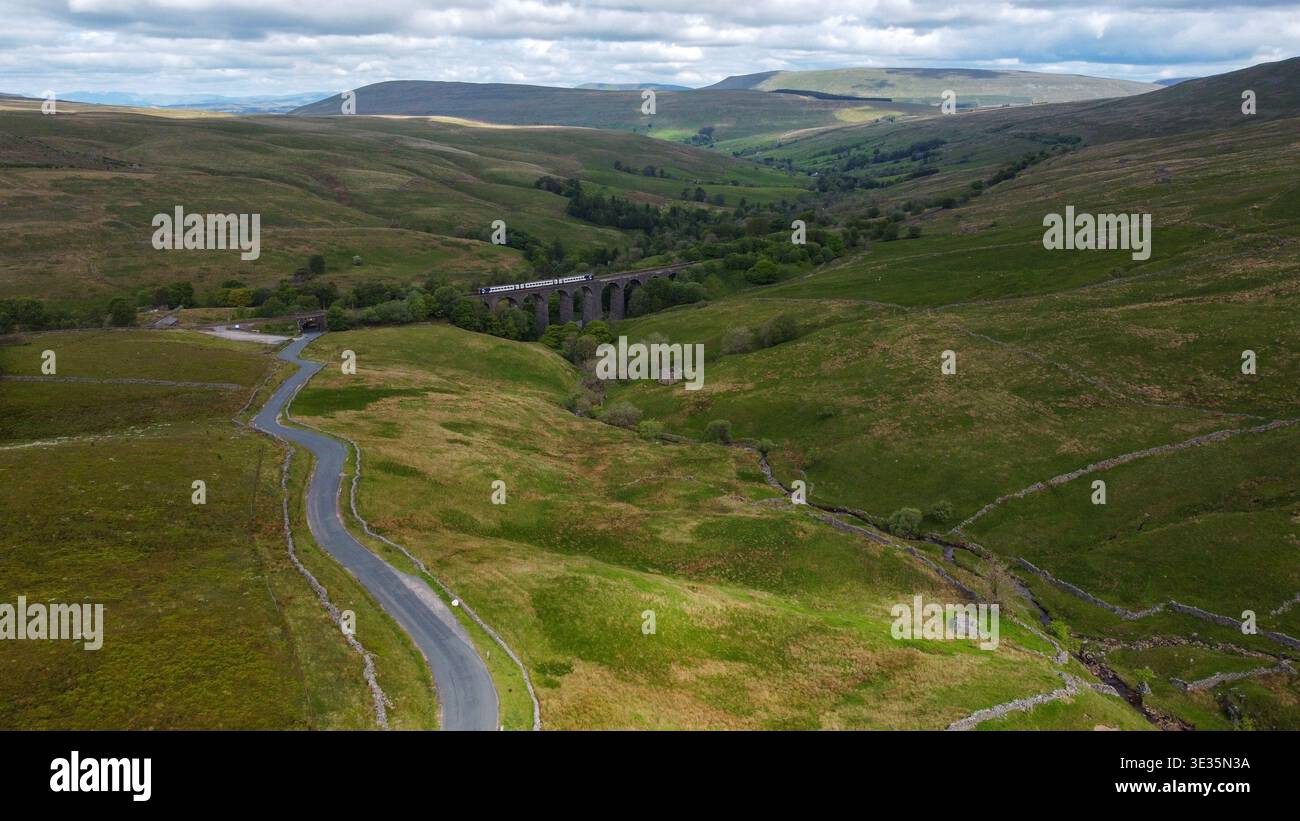 Vista sopraelevata di un treno che attraversa il viadotto di Dent Head e di una tortuosa strada di campagna nelle valli dello Yorkshire Foto Stock