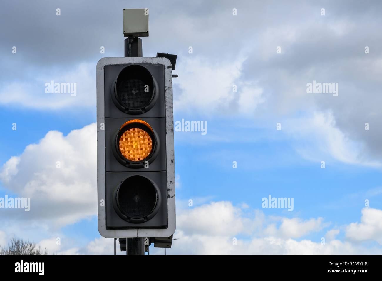 Primo piano del semaforo che mostra un segnale color ambra contro il cielo blu, avvertendo i conducenti di rallentare e prepararsi a fermarsi. Foto Stock