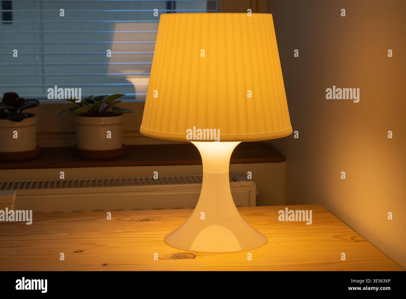 Una calda lampada da tavolo da notte si illumina su un comodino in legno in un ambiente accogliente all'interno della camera da letto. Foto Stock