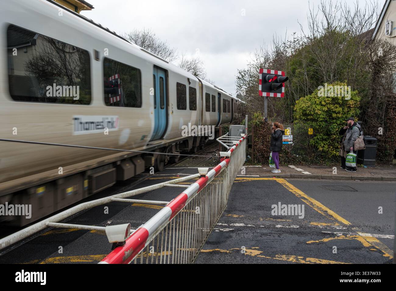 Un treno che collega il Tamigi passando per il passaggio a livello di Crawley Brighton Road, con cancelli in basso e persone in attesa. Foto Stock