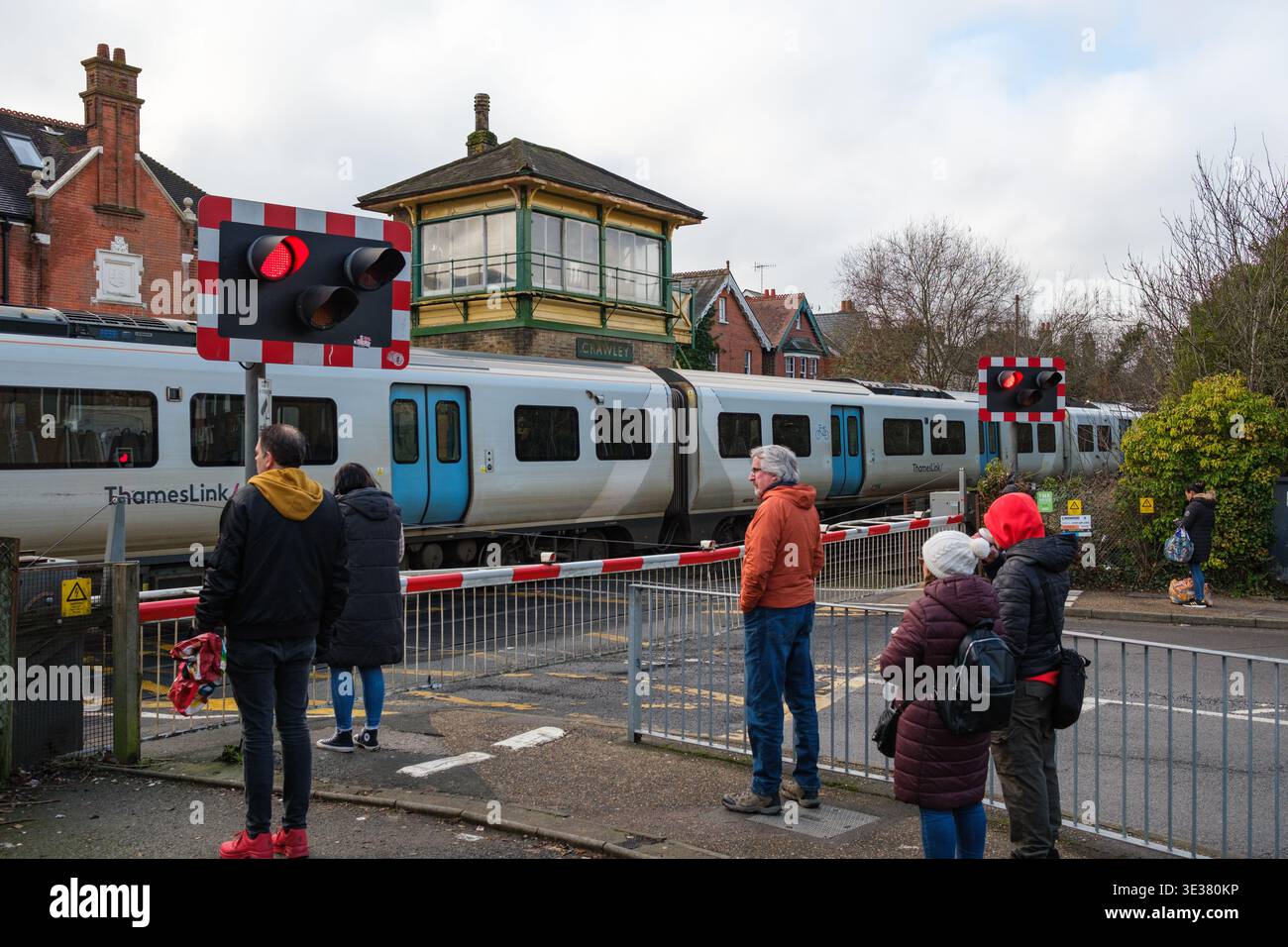 La gente aspetta al passaggio a livello della ferrovia a Crawley Brighton Road, sede della segnaletica vittoriana classificata di secondo livello, mentre passa un treno del Tamigi. Foto Stock