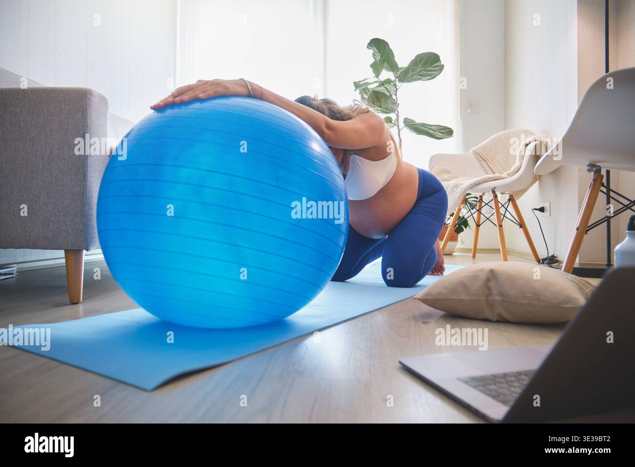 Donna incinta che si allunga su un tappetino da yoga con una palla fitness durante l'allenamento prenatale Foto Stock