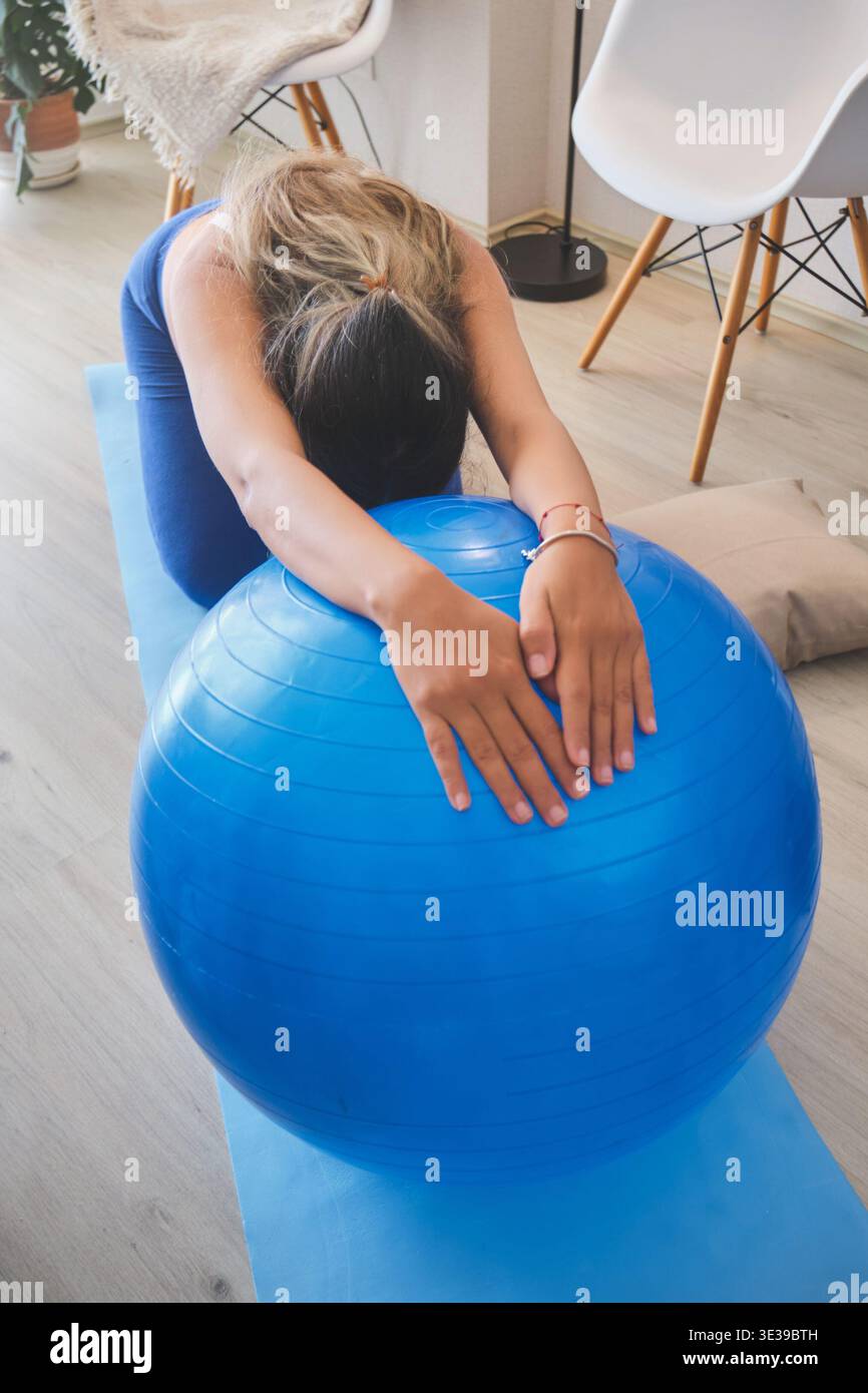 Donna incinta che si allunga su un tappetino da yoga con una palla blu Foto Stock