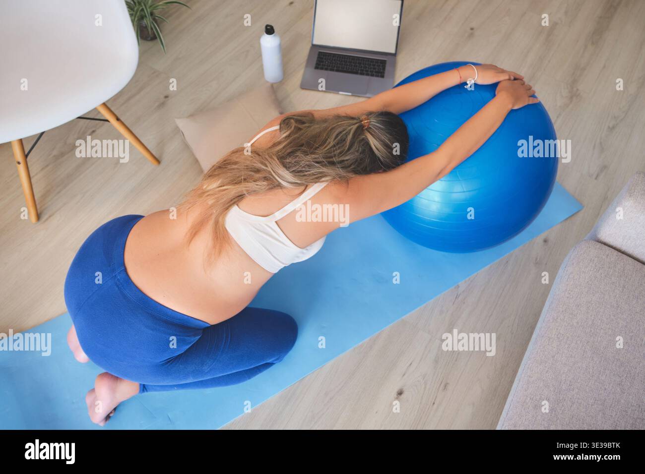 Donna incinta che si allunga su un tappetino da yoga con una palla blu Foto Stock