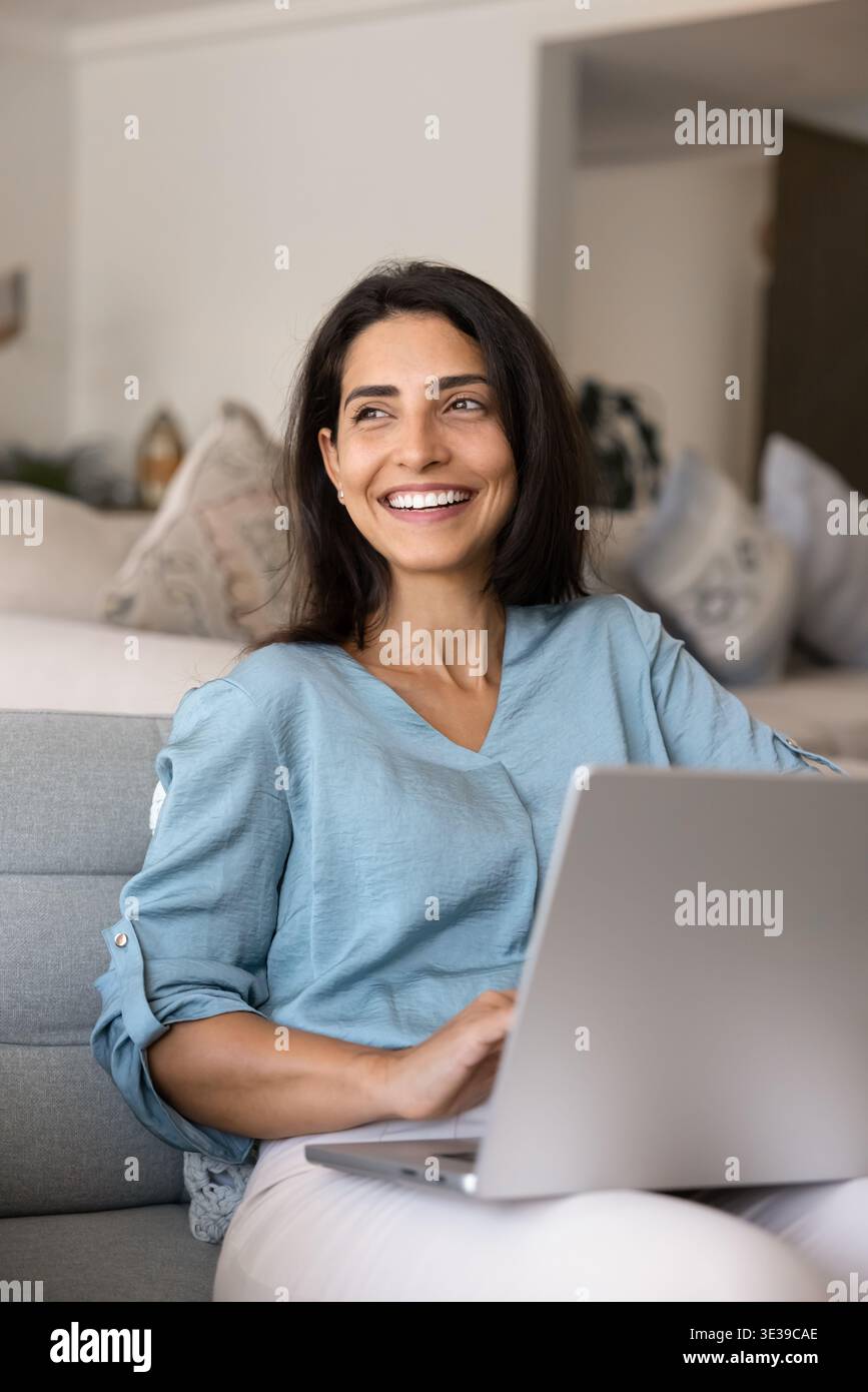 Donna brasiliana sorridente e rilassata che usa un laptop sul divano Foto Stock