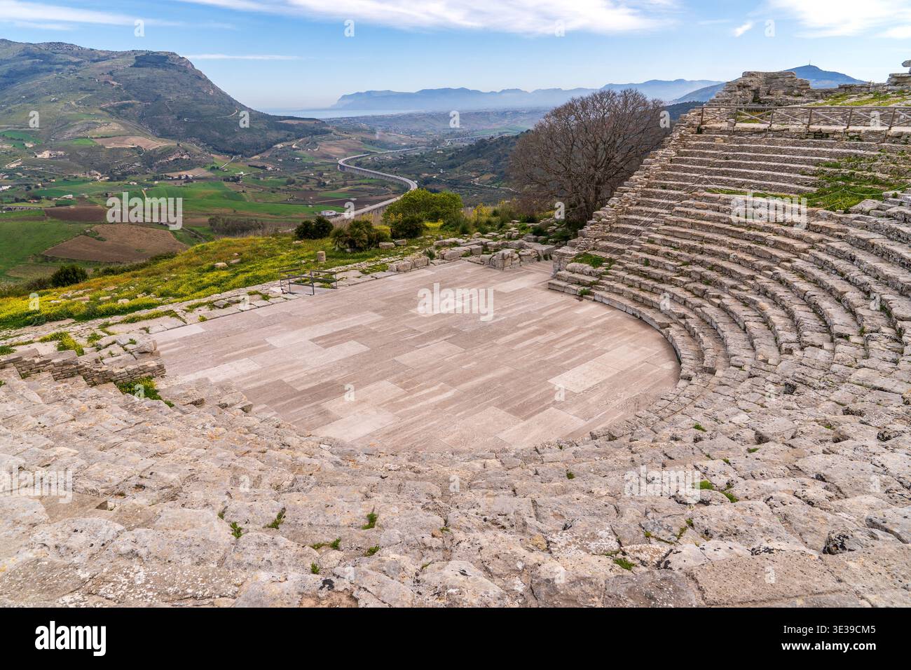 Vista dall'alto del teatro greco di Segesta, Sicilia. I posti a sedere semicircolari in pietra si affacciano su un panorama mozzafiato di colline, fiori gialli e un mod Foto Stock