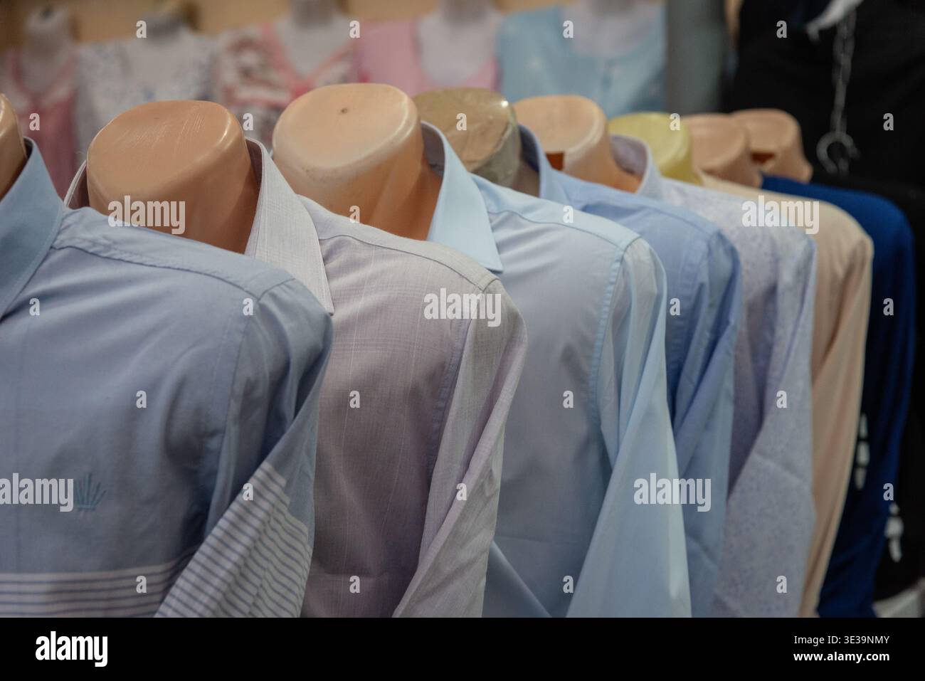 Fila di manichini senza testa che espongono le camicie da uomo in un mercato di abbigliamento, mostrando stili, colori e merchandising al dettaglio. Foto Stock