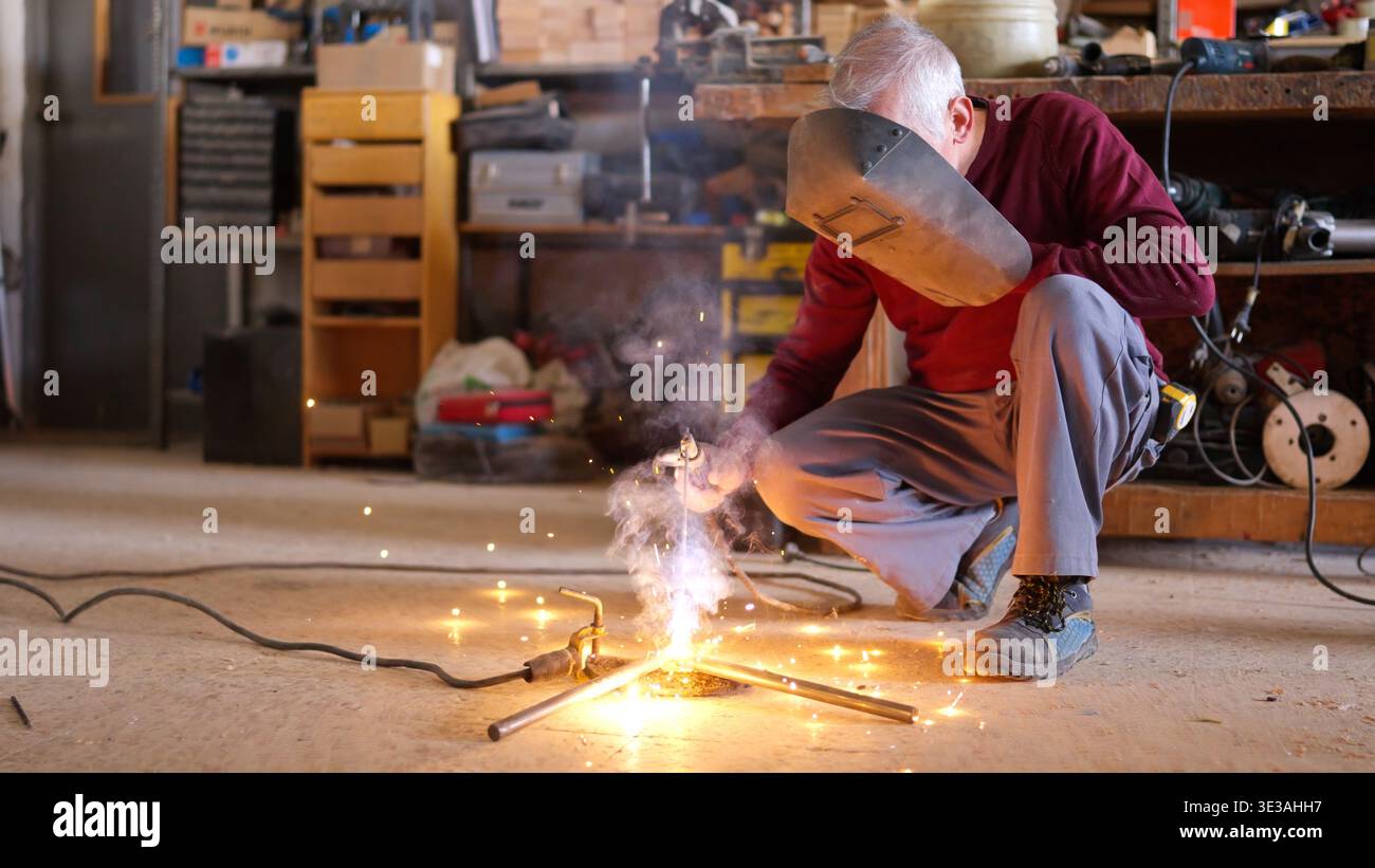 Artigiano senior per la saldatura del metallo in un'officina Foto Stock
