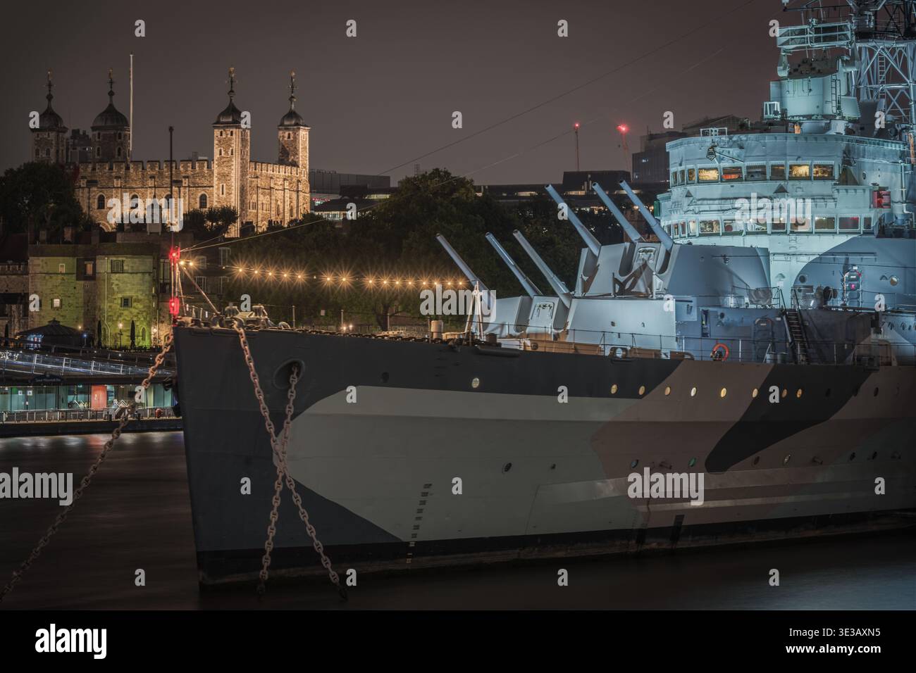 HMS Belfast in primo piano con la Torre illuminata di Londra sullo sfondo Foto Stock