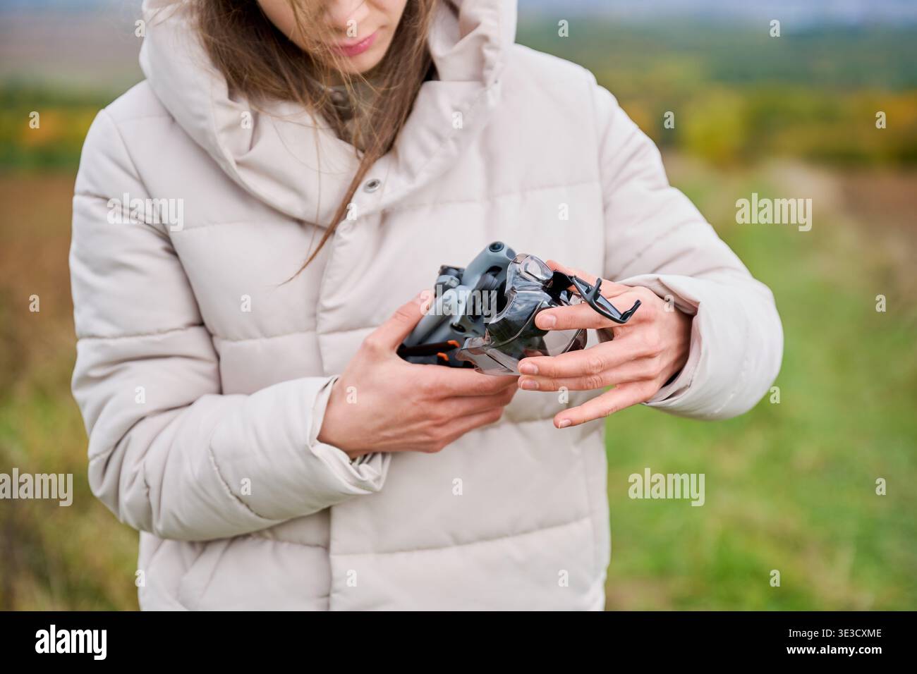 Donna dispiega il drone e rimuove la copertura protettiva. Primo piano sulla preparazione di un quadricottero all'aperto, sulla configurazione delle attrezzature prima del volo, sul concetto di hobby, sulla tecnologia e sull'attività Foto Stock