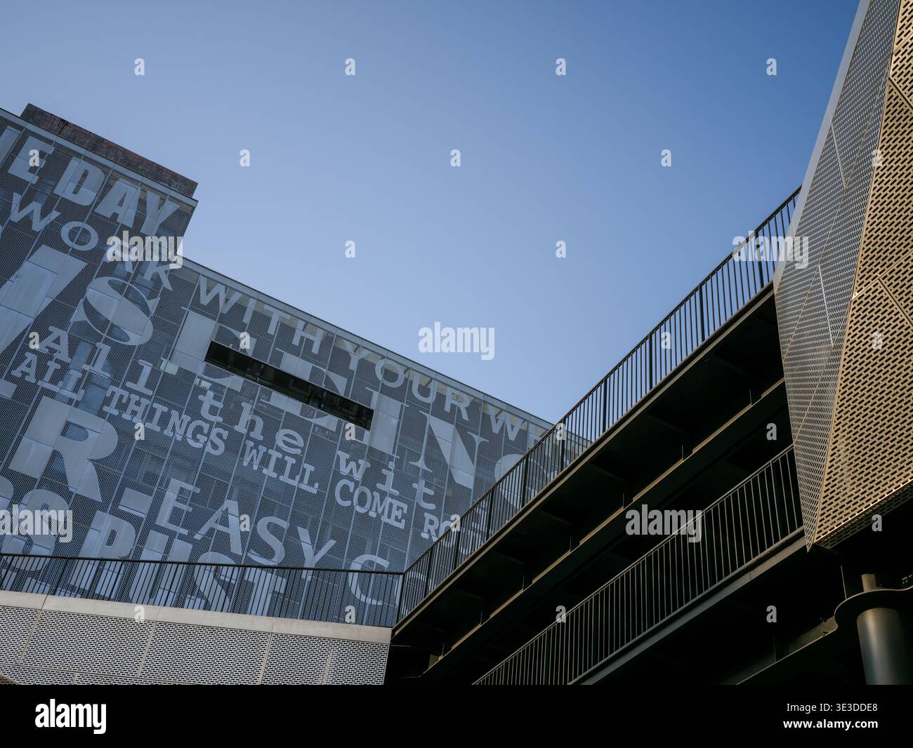 Prospettiva ad angolo basso di una facciata architettonica moderna caratterizzata da una grande tipografia grafica dietro vetro e una scala in metallo perforato contro una clea Foto Stock