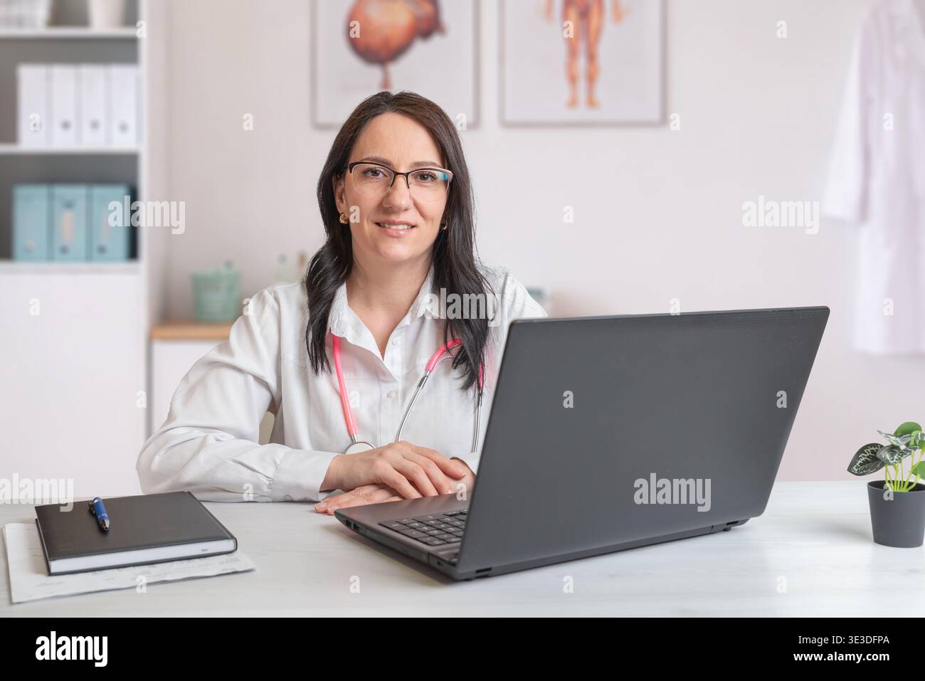 medico che lavora alla scrivania con laptop che guarda la fotocamera che rappresenta il servizio sanitario professionale e la consulenza medica Foto Stock