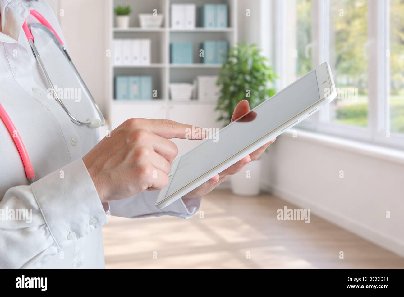 medico che usa il tablet in clinica vicino alla finestra che rappresenta l'assistenza sanitaria digitale, le applicazioni mediche e i servizi di telemedicina Foto Stock